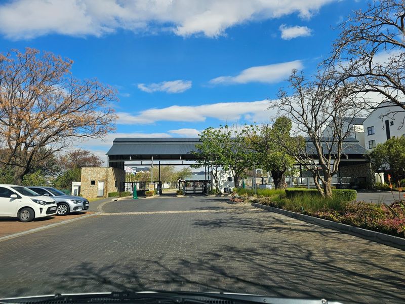 View of the secure entrance gatehouse and paved driveway leading into the apartment complex, featuring stone cladding and established landscaping.