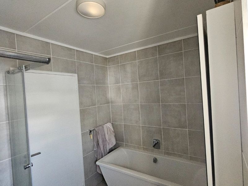 A functional bathroom featuring a bathtub, a separate glass-enclosed shower, and a wall-mounted basin with neutral ceramic tiling throughout.