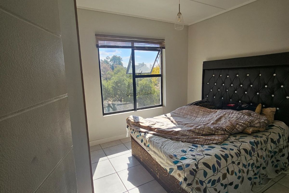 A bedroom featuring tiled flooring, a top-hung window with a venetian blind, and a central pendant light fitting.