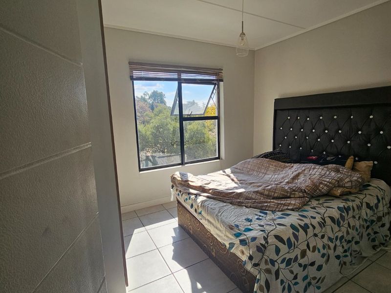 A bedroom featuring tiled flooring, a top-hung window with a venetian blind, and a central pendant light fitting.