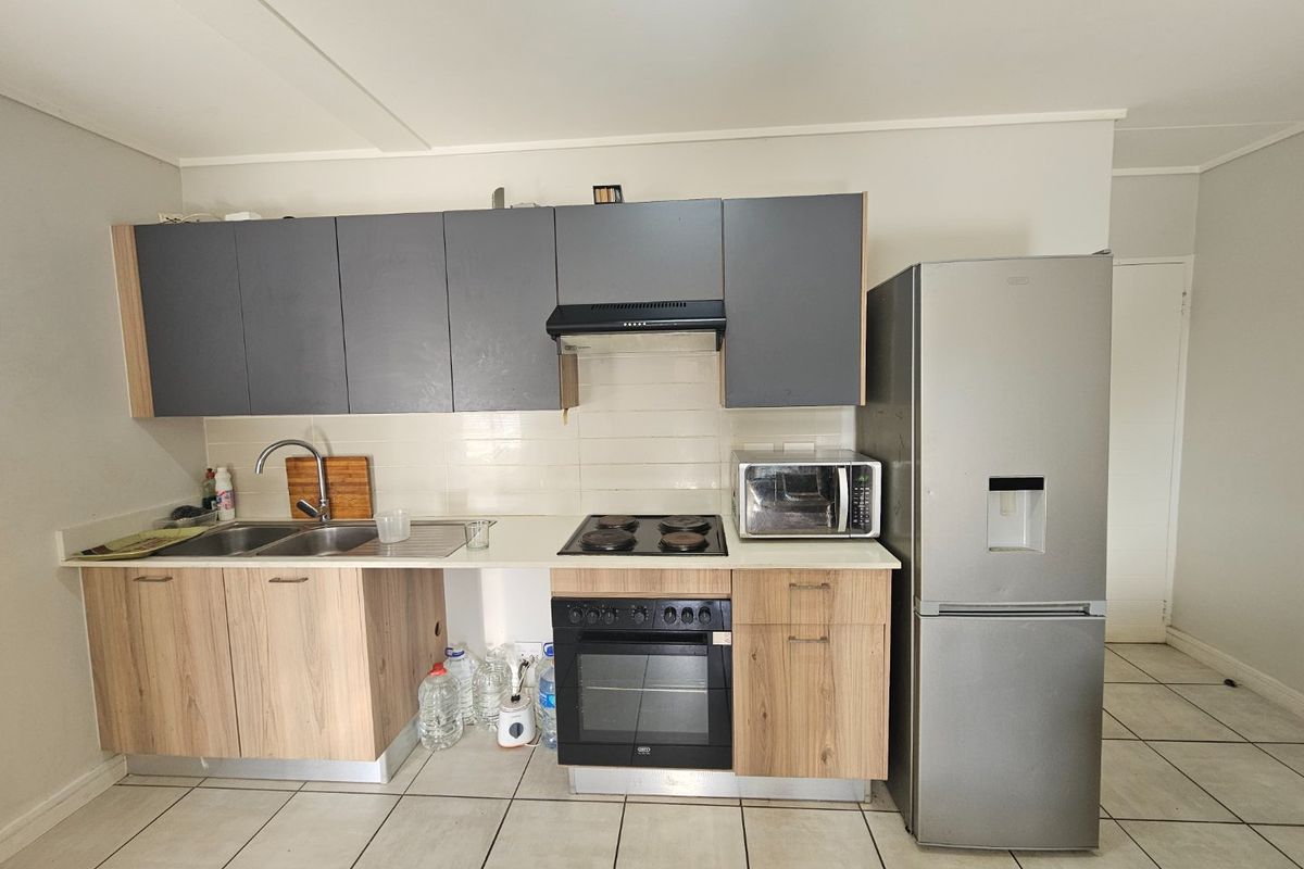 A functional kitchen featuring wood-look lower cabinets, grey upper cabinets, tiled backsplash, and integrated cooking appliances with tiled flooring throughout.