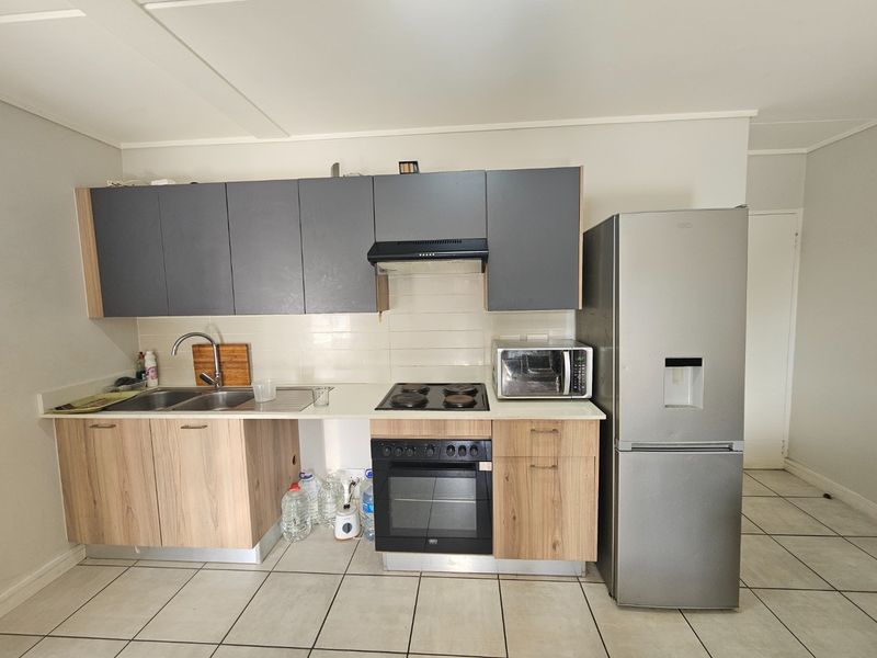 A functional kitchen featuring wood-look lower cabinets, grey upper cabinets, tiled backsplash, and integrated cooking appliances with tiled flooring throughout.