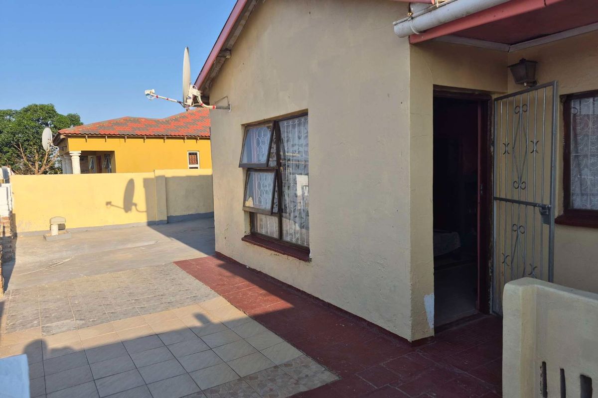 Rear exterior view of the house featuring a tiled patio area, security gate, and satellite dish installation.