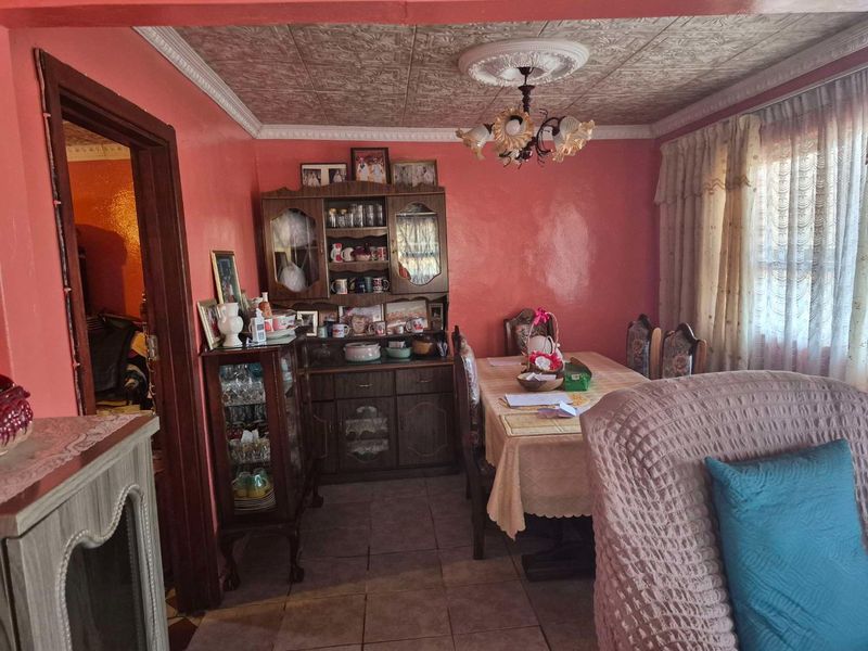 A dining room featuring decorative ceiling tiles, a central ceiling rose, and tiled flooring, currently styled with traditional cabinetry and furnishings.