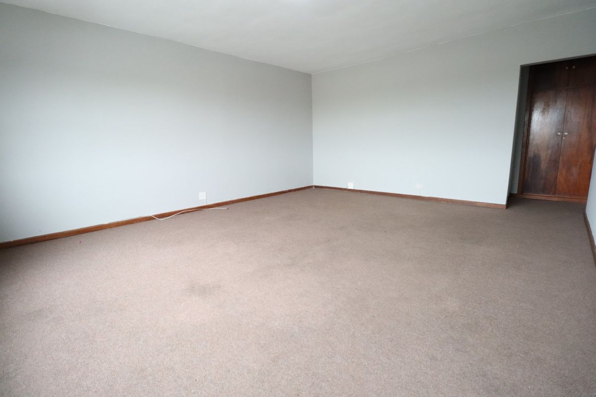 An empty bedroom featuring neutral walls, carpeted flooring, and built-in wooden cupboards, offering a blank canvas for personalization.