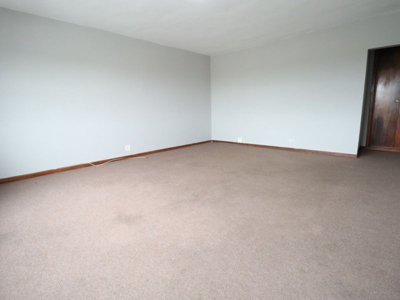 An empty bedroom featuring neutral walls, carpeted flooring, and built-in wooden cupboards, offering a blank canvas for personalization.