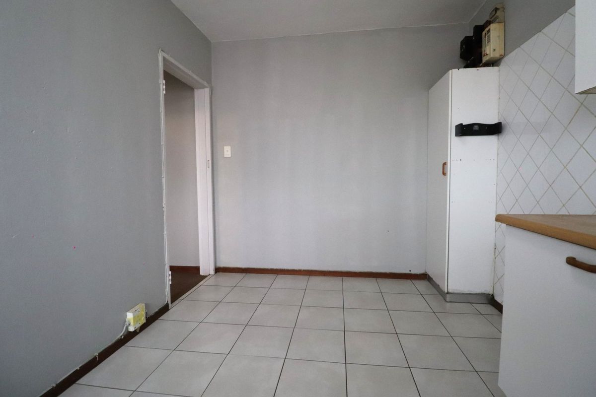 A compact, empty kitchen area featuring tiled flooring, neutral grey walls, and basic built-in cabinetry with a tiled backsplash.