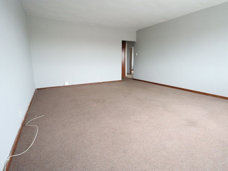 A spacious, empty living room featuring neutral wall paint, carpet flooring, and wooden skirting boards, offering a blank canvas for interior design.