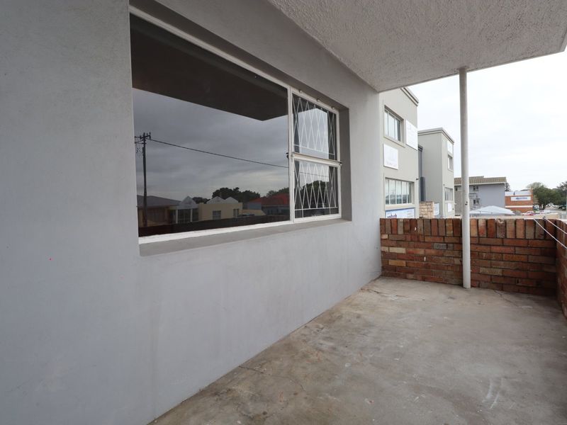 A covered balcony featuring a brick balustrade, metal support column, and concrete flooring, offering a functional outdoor space.
