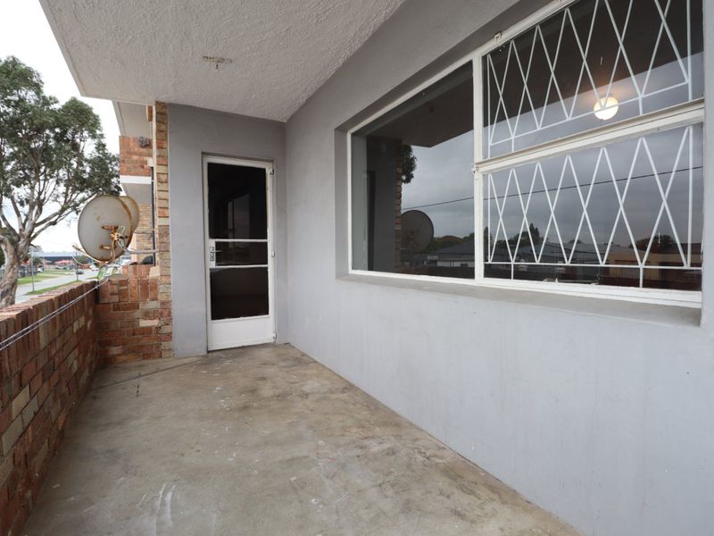 A covered balcony area featuring a brick balustrade, security gate, and security bars on the window, offering a functional outdoor space.