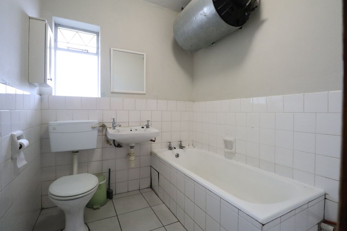 A functional bathroom featuring a bathtub, pedestal basin, and toilet, with white wall tiling and an exposed electric water heater.