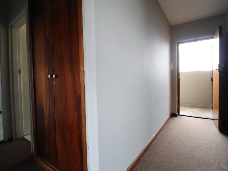 A functional hallway featuring a built-in wooden cupboard, intercom system, and carpeted flooring, providing access to adjacent rooms and an exterior balcony.