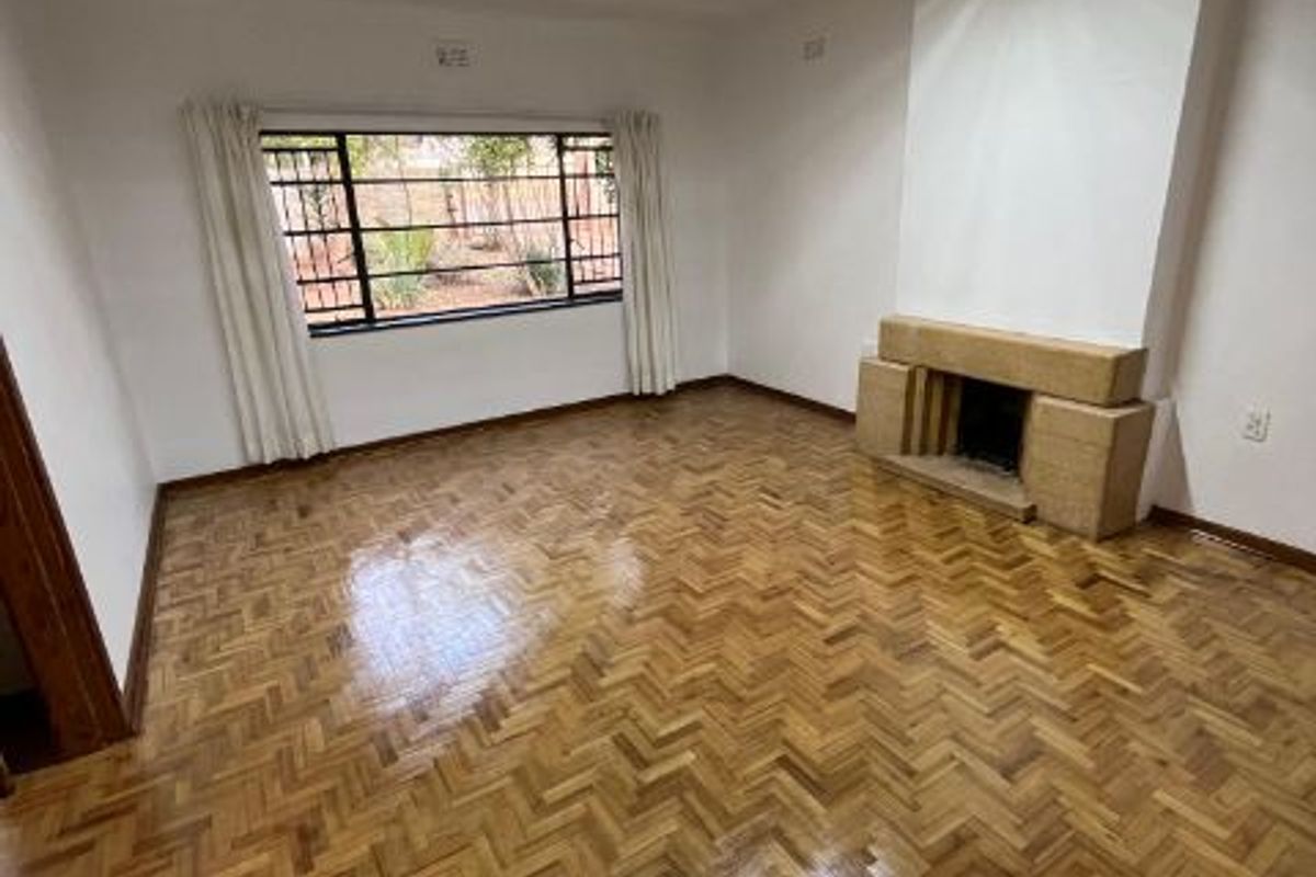 Spacious living room featuring polished herringbone parquet flooring, a built-in fireplace, and large windows with security bars.