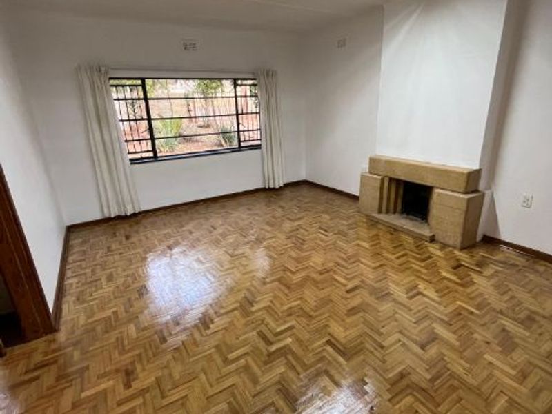 Spacious living room featuring polished herringbone parquet flooring, a built-in fireplace, and large windows with security bars.