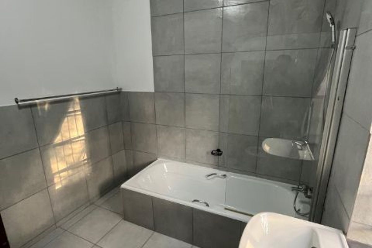 A modern bathroom featuring grey floor-to-ceiling wall tiles, a built-in bathtub with a glass shower screen, and a pedestal basin.
