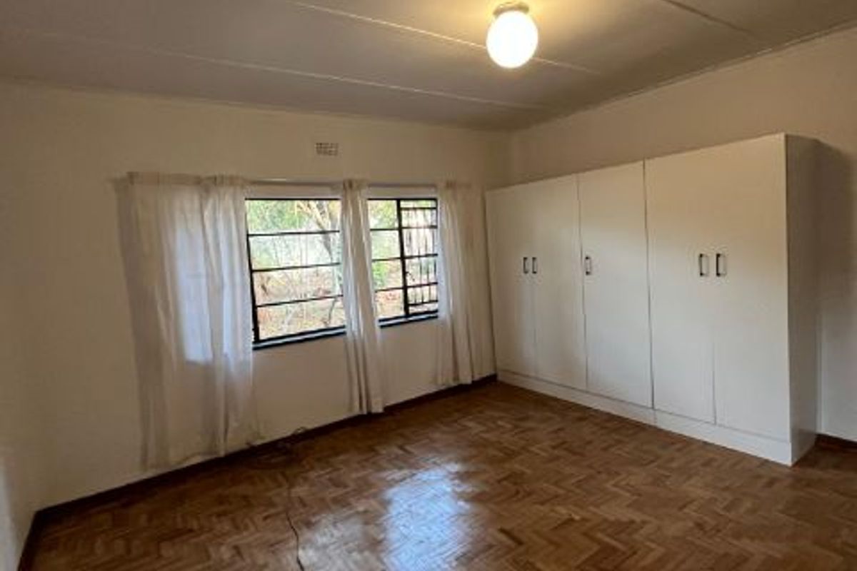 Spacious bedroom featuring polished parquet flooring, built-in cupboards, and large steel-framed windows allowing for natural light.