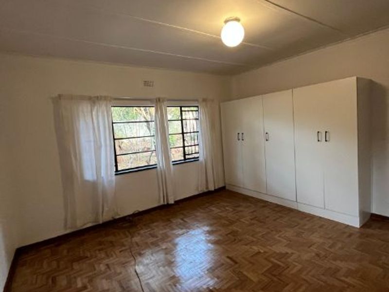 Spacious bedroom featuring polished parquet flooring, built-in cupboards, and large steel-framed windows allowing for natural light.