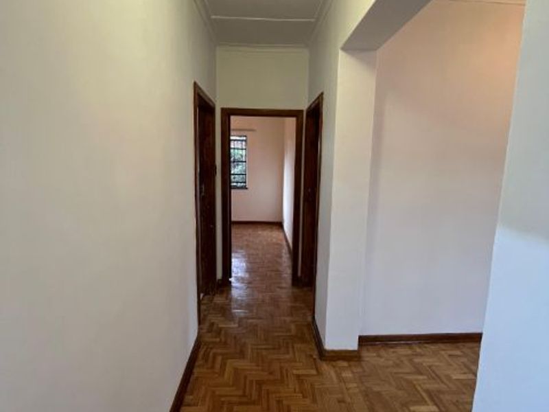 A bright, empty hallway featuring classic parquet flooring and wooden door frames, leading into adjacent rooms.