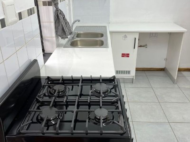 A functional kitchen area featuring a gas stove, double basin sink, tiled splashbacks, and tiled flooring with ample counter space.