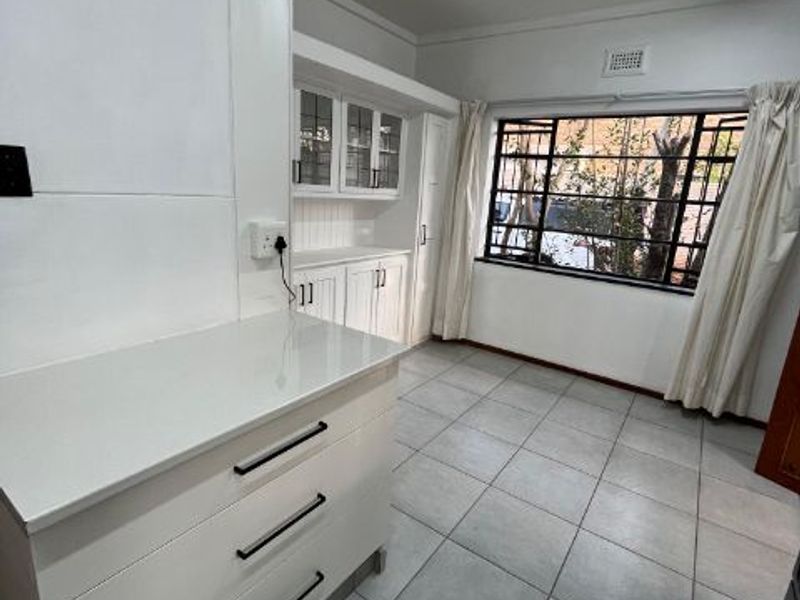 A clean, functional scullery or utility area featuring white built-in cabinetry, tiled flooring, and a large window with security bars.