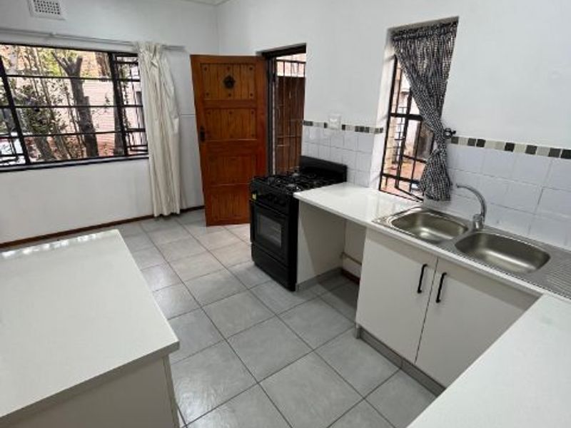 A functional kitchen featuring white cabinetry, stone countertops, a double bowl sink, and a freestanding gas stove with tiled flooring throughout.