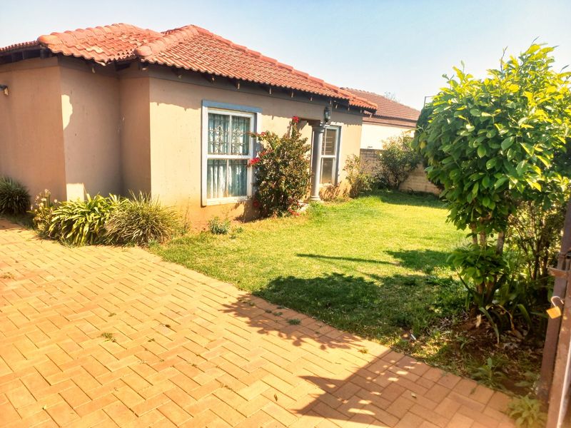 Front view of a single-story house featuring a terracotta tiled roof, paved driveway, and a small front garden area.