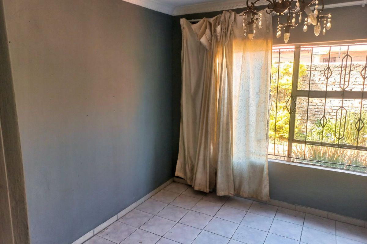 An empty bedroom featuring tiled flooring, security bars on the window, and a decorative chandelier, awaiting a fresh coat of paint and updates.