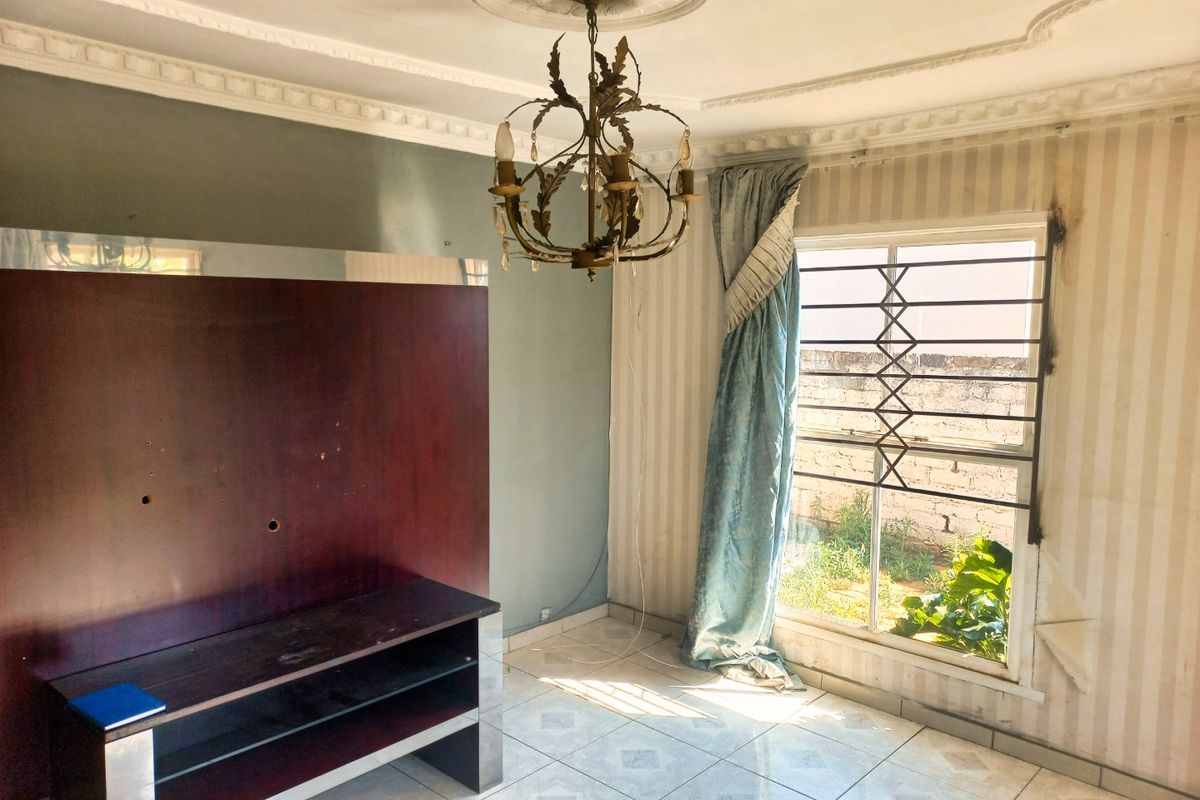 Living room featuring tiled flooring, decorative ceiling rose, and built-in media cabinetry, requiring cosmetic updates to address wall damage and dated finishes.