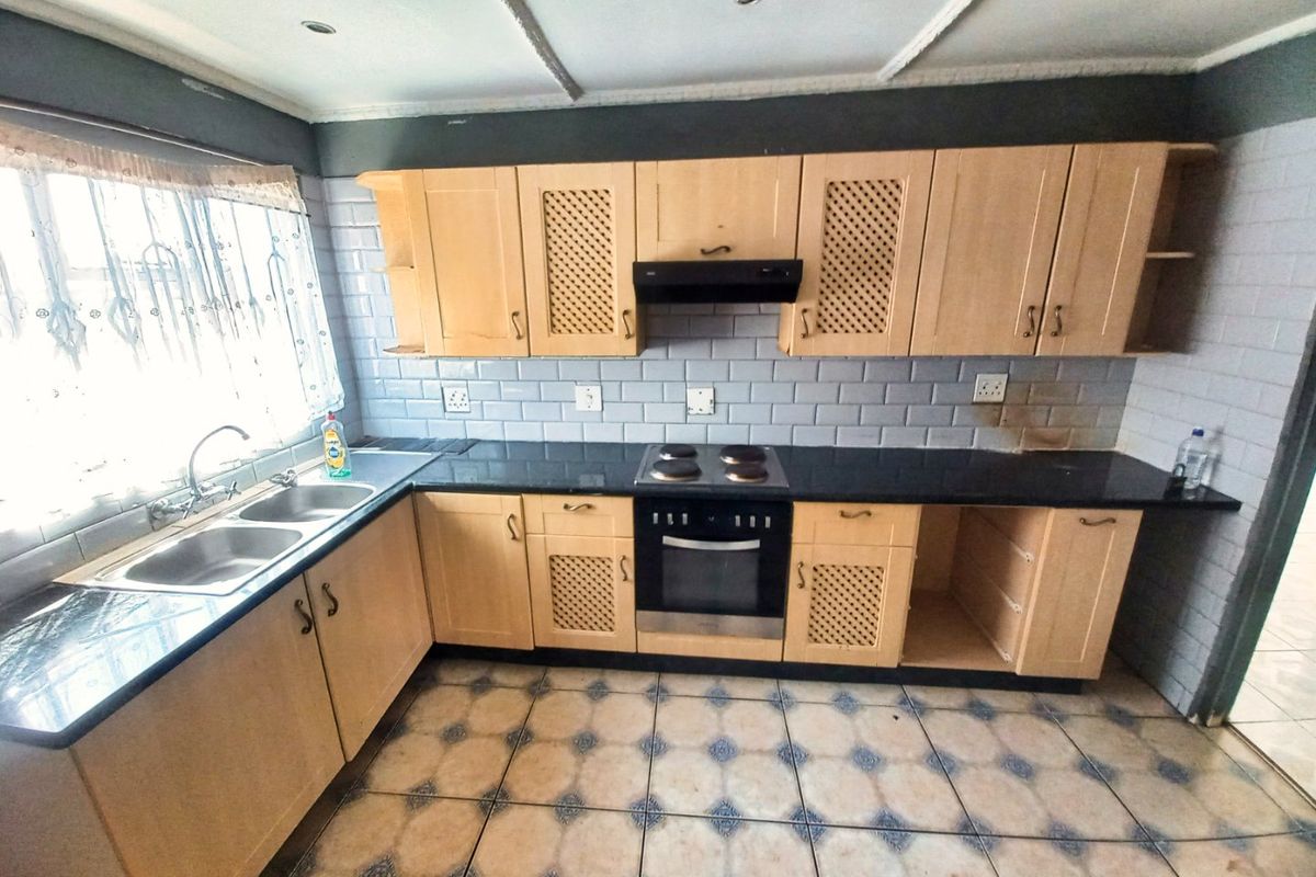 A functional kitchen featuring light wood cabinetry, black granite countertops, a built-in oven with hob, and a double basin sink with subway tile backsplash.