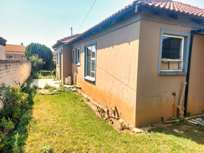 Rear view of the house featuring a small paved patio, lawn area, and boundary wall, showing signs of exterior wear and maintenance requirements.