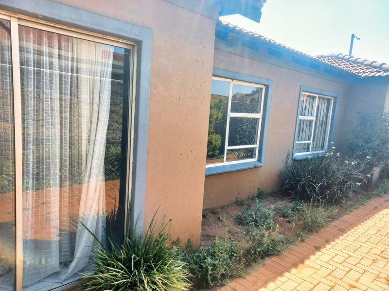 Rear exterior view of the house featuring a sliding glass door, aluminium windows with security bars, and a brick paved walkway.