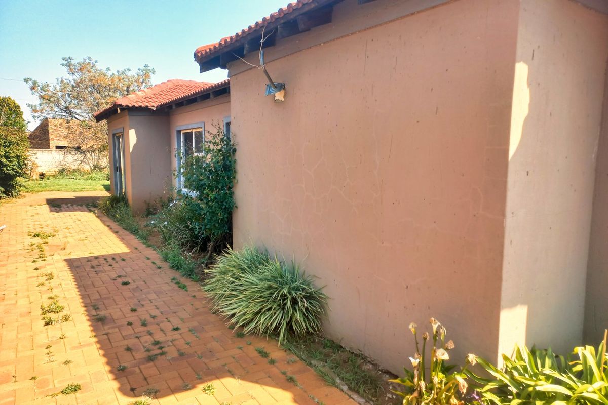 A view of the rear exterior of the house featuring a paved walkway, terracotta roof tiles, and visible hairline cracks on the exterior wall.