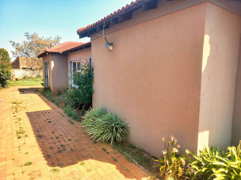 A view of the rear exterior of the house featuring a paved walkway, terracotta roof tiles, and visible hairline cracks on the exterior wall.