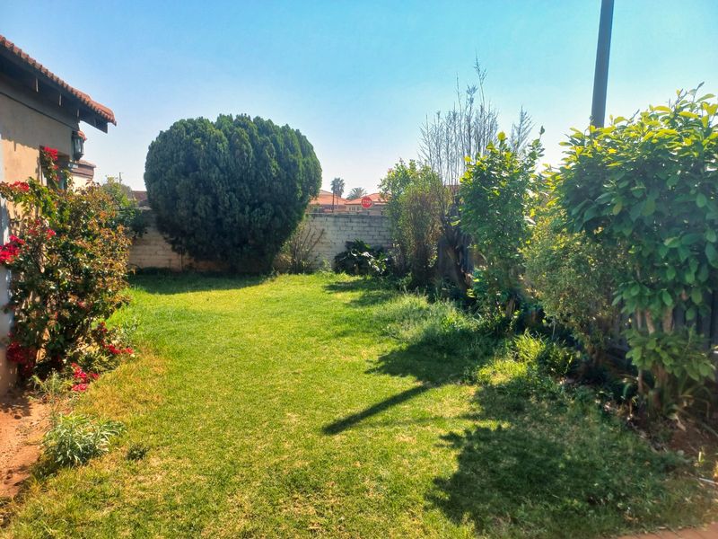 A private rear garden featuring a well-maintained lawn, established shrubs, and a perimeter boundary wall.