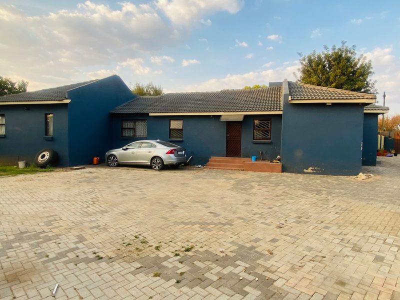 Front exterior view of a single-story house featuring a paved driveway, tiled roof, and blue painted facade with security features.