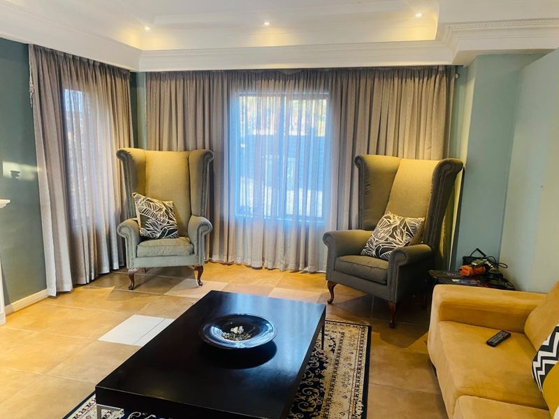 A living room featuring tiled flooring, recessed ceiling with cove molding, and recessed downlights, providing a comfortable and well-lit space.