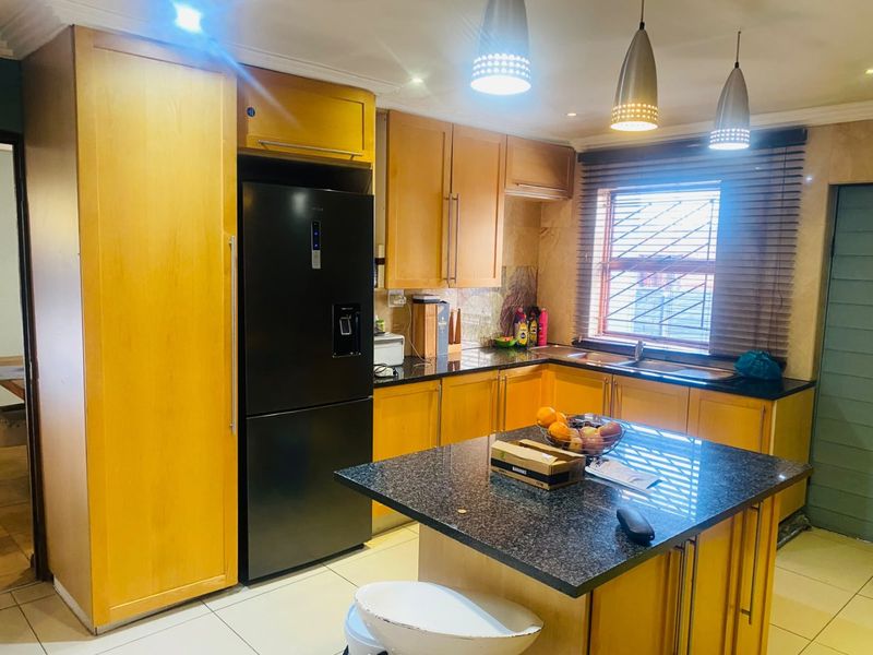 A functional kitchen featuring warm-toned wooden cabinetry, granite countertops, a central island, and tiled flooring, illuminated by modern pendant lighting.