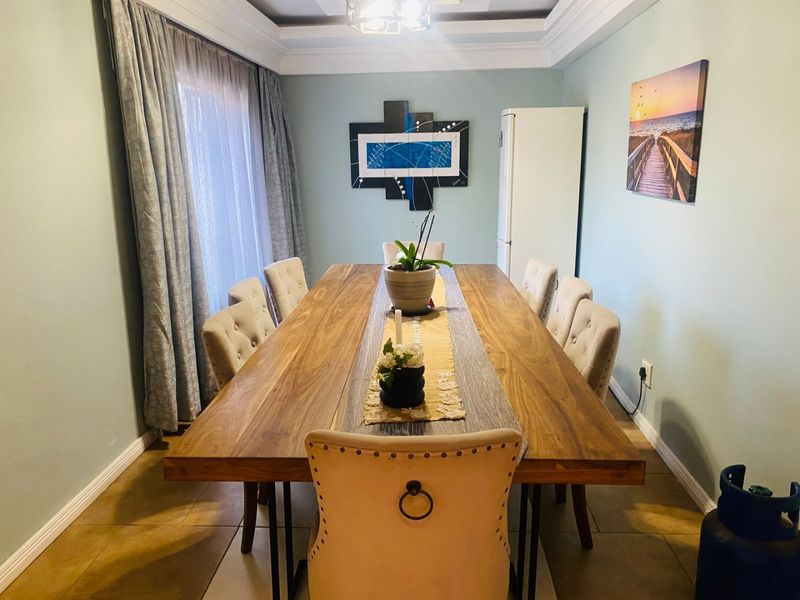A well-maintained dining room featuring tiled flooring, a decorative tray ceiling with crown molding, and large windows with floor-to-ceiling curtains.