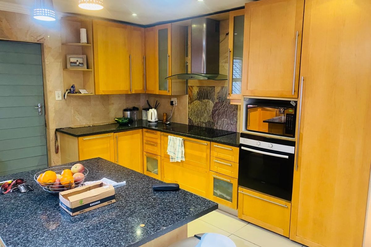 A functional kitchen featuring warm-toned wooden cabinetry, granite countertops, a central island, and integrated appliances including an oven and microwave.