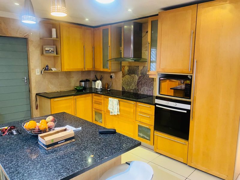 A functional kitchen featuring warm-toned wooden cabinetry, granite countertops, a central island, and integrated appliances including an oven and microwave.