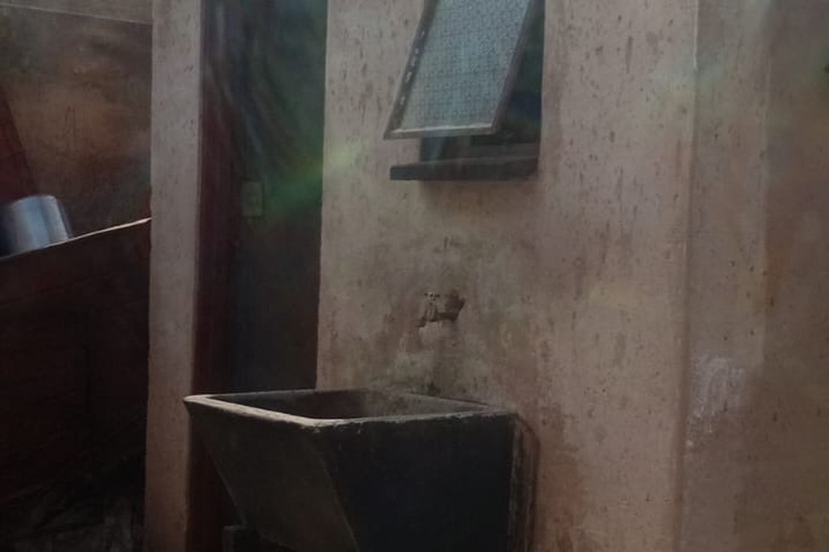 An outdoor utility area featuring a concrete sink, tiled flooring, and an exterior door, showing signs of significant weathering and wear.