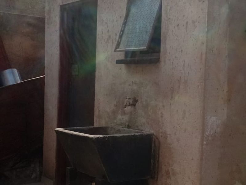 An outdoor utility area featuring a concrete sink, tiled flooring, and an exterior door, showing signs of significant weathering and wear.