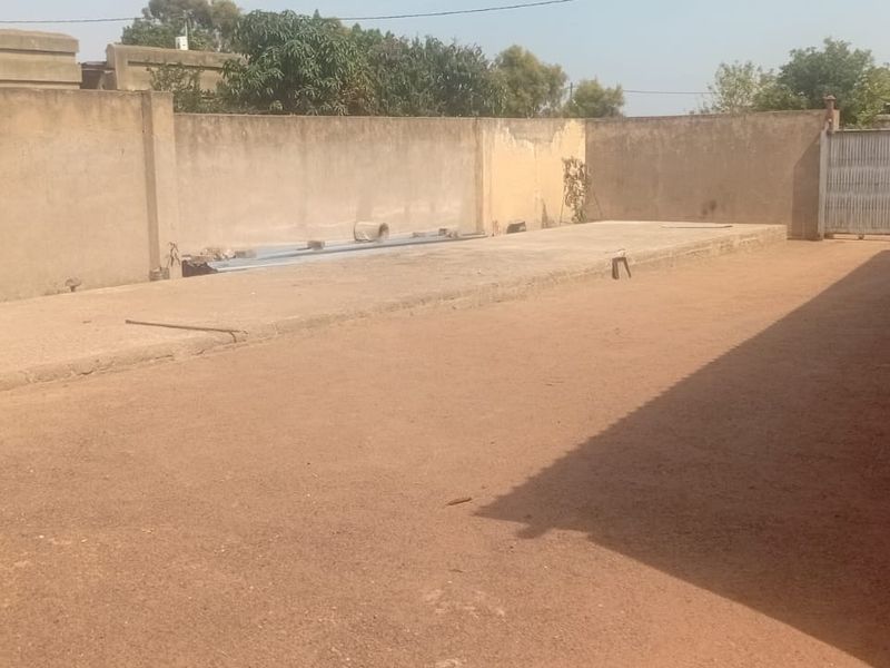 A spacious, unpaved rear yard area enclosed by a perimeter wall, featuring a metal sliding gate and a concrete slab foundation.