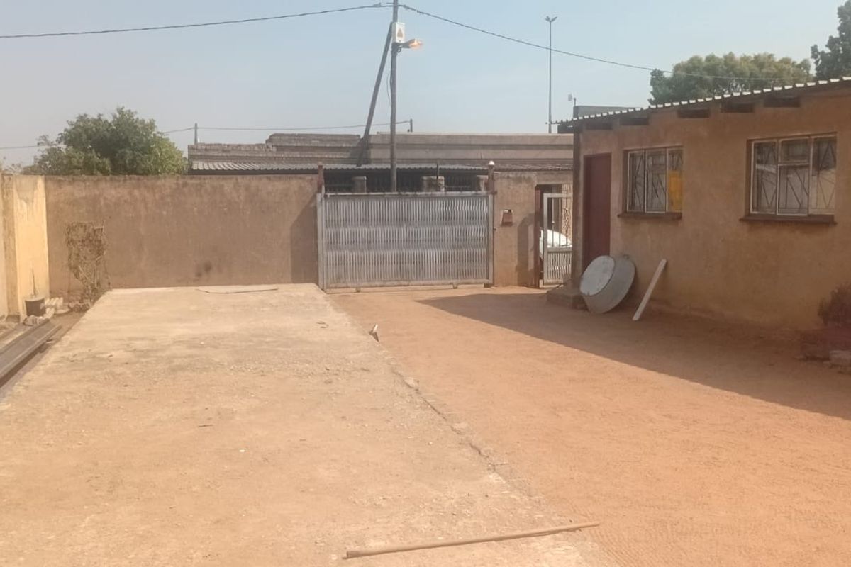 Rear exterior view showing a concrete driveway, perimeter wall, and the side facade of the building with steel window frames.