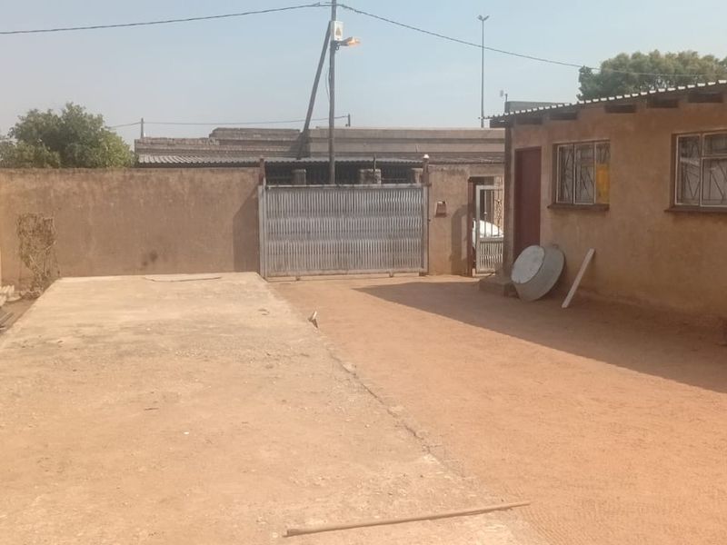 Rear exterior view showing a concrete driveway, perimeter wall, and the side facade of the building with steel window frames.