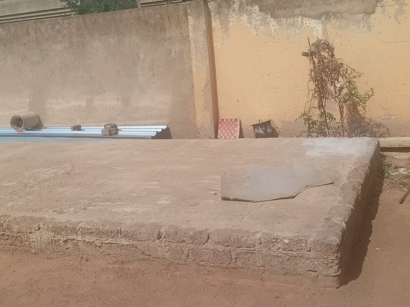 A rear outdoor area featuring a raised concrete slab foundation enclosed by a weathered perimeter boundary wall.