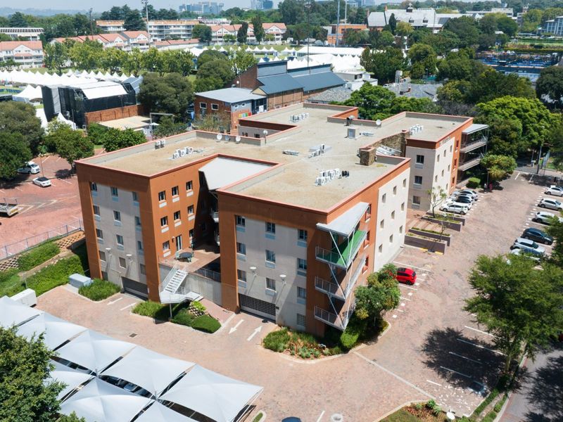 Aerial view of a multi-story commercial building featuring a flat roof, external staircases, balconies, and an extensive paved parking area.