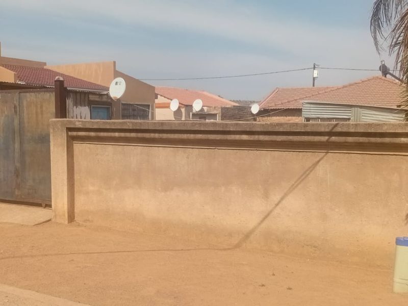 Front view of the property featuring a perimeter boundary wall and a metal driveway gate, showing standard residential exterior finishes.