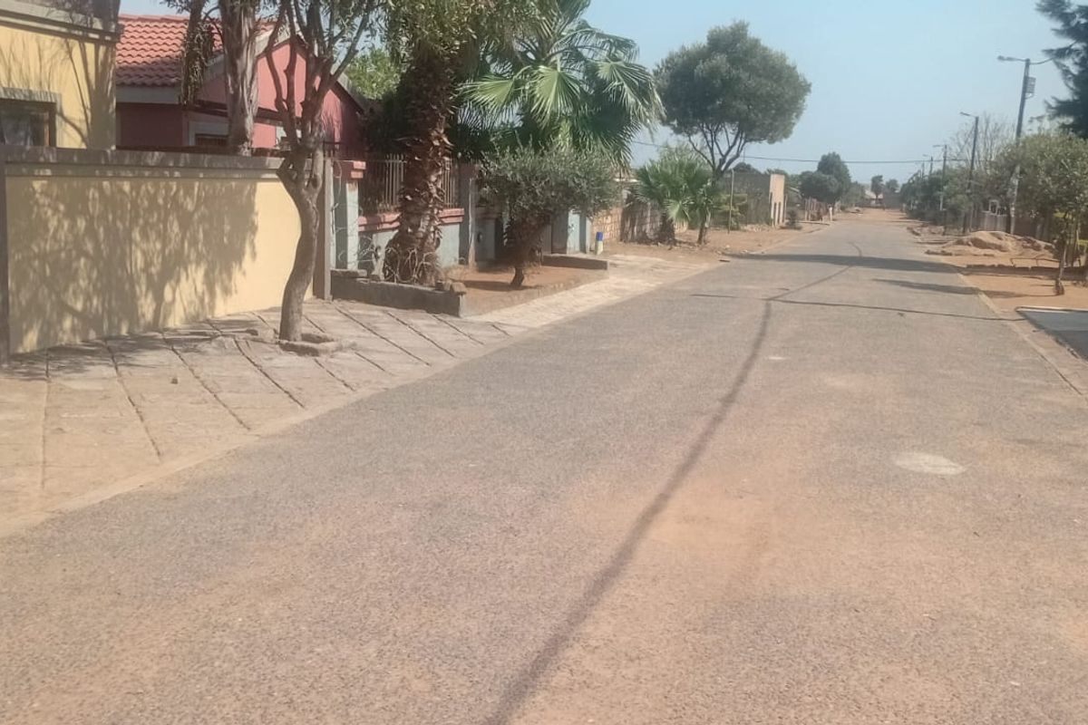 A view of the residential street showing the paved road, sidewalk, and boundary wall of the property.