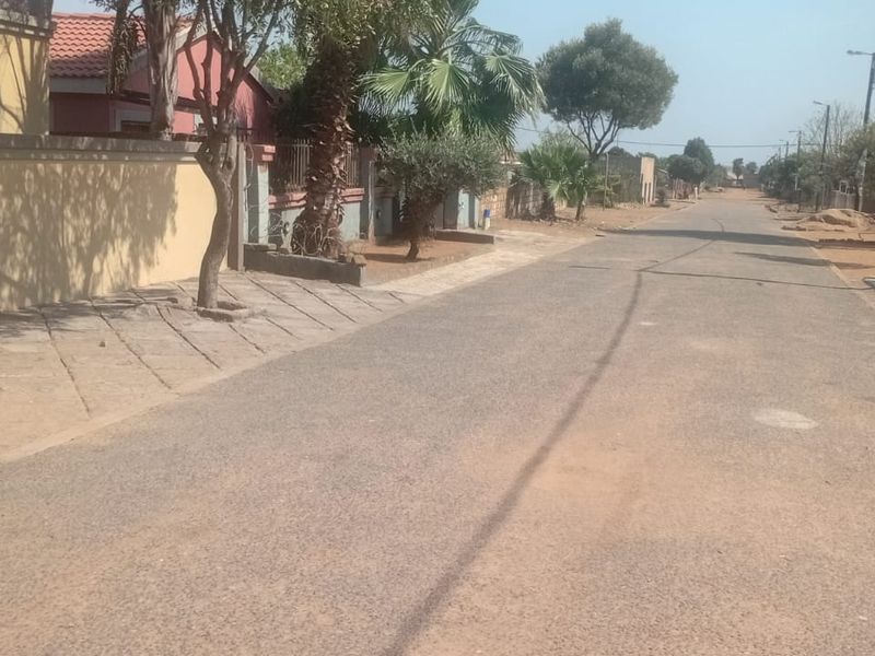 A view of the residential street showing the paved road, sidewalk, and boundary wall of the property.